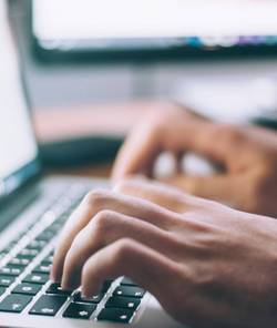man's fingers writing on a laptop